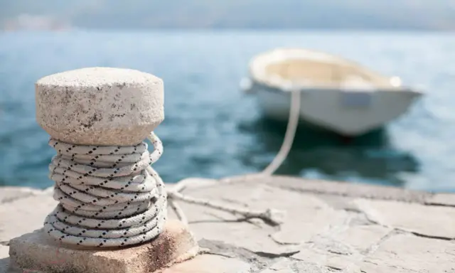 Un cordage est enroulé autour d'une borne en pierre sur un quai, prêt pour le prochain pendille bateau.