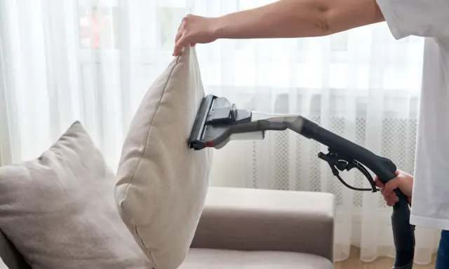 En person dammsuger soffa och kuddar för att få bort damm och smuts.