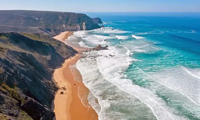 Atemberaubende Küstenlandschaft im Distrikt Faro, Portugal. Steile Klippen treffen auf einen goldenen Sandstrand und das türkisfarbene Meer mit tosenden Wellen.