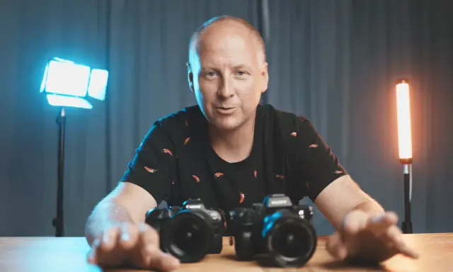 Mężczyzna z aparatami przed sobą, gotowy do rozpoczęcia kursu fotografii.