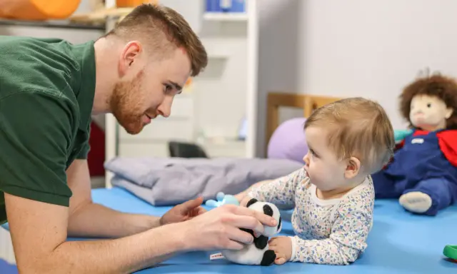Osteopata dla dzieci delikatnie bawi się z niemowlęciem pluszową pandą, wspierając jego rozwój.