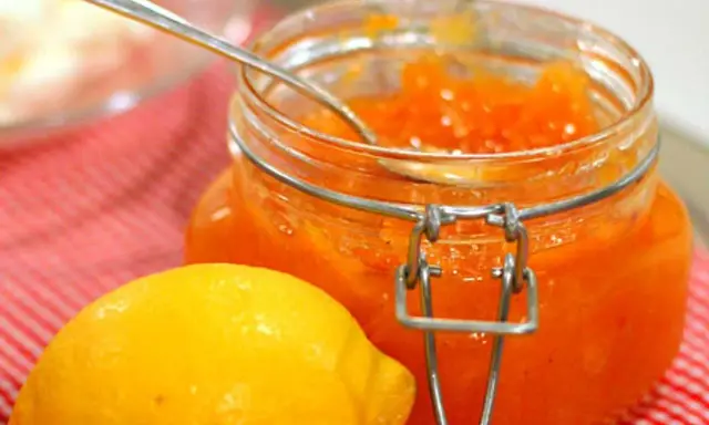 En burk med hemgjord citronmarmelad och en färsk citron på en rödvitrutig duk.