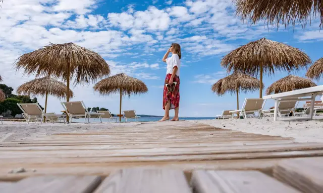 Kobieta na plaży, pod słomianymi parasolami, podziwia widok. To idealne miejsce na wyspie Rab, atrakcje czekają!