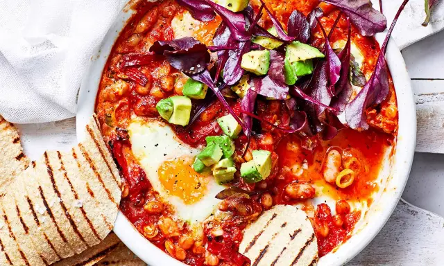 Herzhaftes Gericht mit pochierten Eiern in Tomatensoße, Bohnen, Avocado und Rotkohl. Perfekt für gesunde Rezepte Abendessen. Dazu geröstetes Fladenbrot.