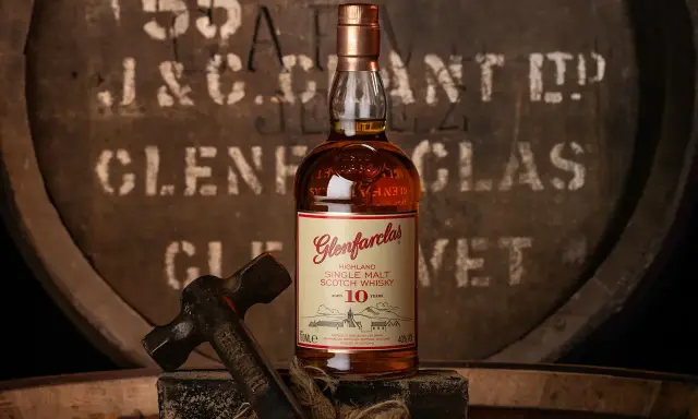 Butelka Glenfarclas 10 Year Old, jedna z 10 najlepszych whisky, na tle beczki. Młotek sugeruje rzemiosło.