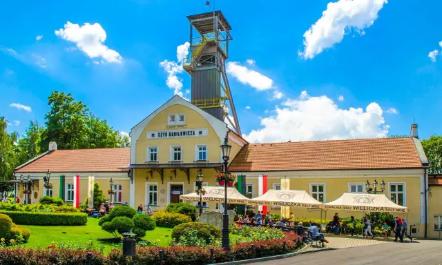 Wieliczka atrakcje: Szyb Daniłowicza, żółte budynki kopalni, zielony ogród i ludzie odpoczywający pod namiotami.
