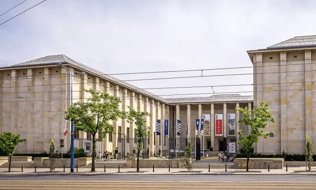Warszawa: monumentalny budynek Muzeum Narodowego z flagami i drzewami przed wejściem.