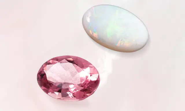 Due gemme ovali, una rosa e un opale, brillano su sfondo chiaro. La pietra rosa ricorda la pietra d'ottobre.