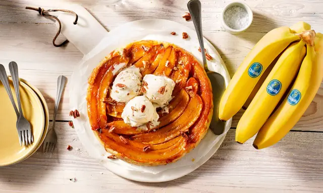 Tarte banane caramel beurre salé, garnie de boules de glace à la vanille et de noix de pécan. Des bananes Chiquita sont à côté.