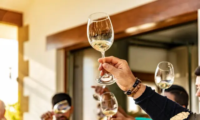Manos brindando con copas de vino blanco. ¿Qué es chacolí? Es un vino joven y fresco, ideal para disfrutar en buena compañía.