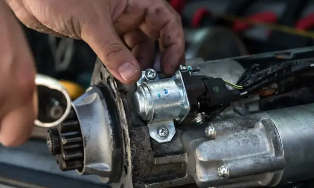 Mechanik naprawia rozrusznik w aucie, przykręcając element.
