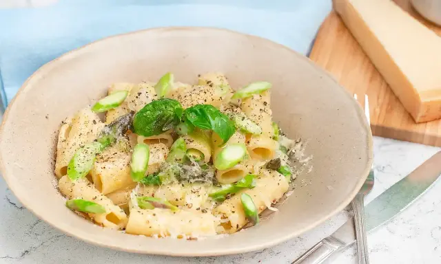 Creamy pasta with asparagus, basil, and grated parmesan cheese in a bowl, with a wedge of parmesan on a cutting board.