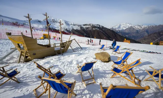 Alpe di Mera: un galeone di legno e sdraio blu attendono i visitatori sulla neve, con montagne innevate sullo sfondo.