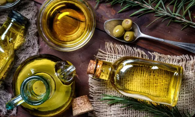 Aceite de oliva en botellas y cuenco, con aceitunas y romero. A pesar de sus beneficios, hay desventajas del aceite de oliva, como su precio.