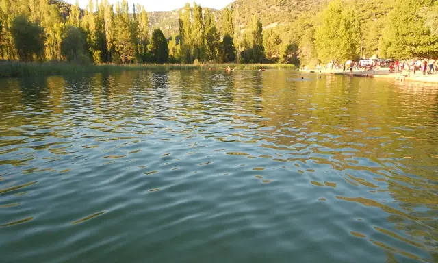 Gente disfrutando del agua en la playa de Cañamares, rodeada de árboles y montañas.