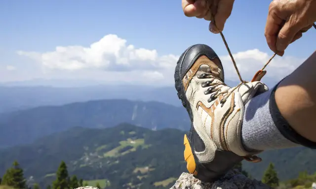 Ręka zawiązuje sznurówki buta trekkingowego na tle górskiego krajobrazu. Właściwe wiązanie butów to klucz do komfortowej wędrówki.