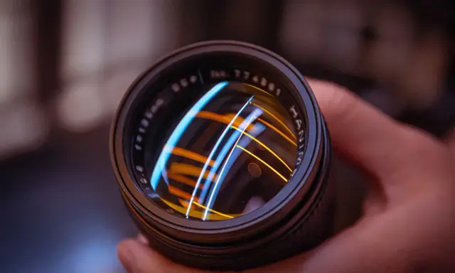 Primer plano de un objetivo fotográfico con reflejos de luces azules y naranjas.