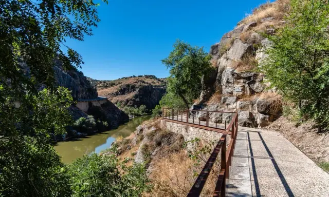 Sendero con barandilla de metal junto a un río y rocas, ideal para rutas senderismo Toledo.