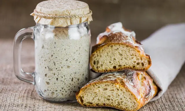 Un bocal de levain actif, prêt à être utilisé pour entretenir son levain, à côté de deux belles tranches de pain artisanal.