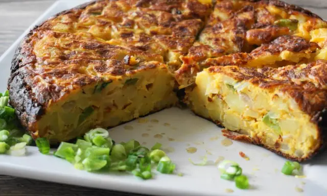 Pyszna tortilla de patatas, pokrojona na kawałki, z zieloną cebulką na talerzu.