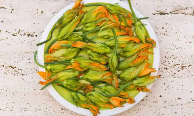 Fiori di zucca freschi, pronti per essere cucinati in padella, su un piatto bianco.