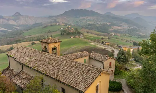 Borghi collinari perfetti per gite in giornata da Reggio Emilia. Un campanile svetta tra tetti antichi e dolci pendii verdi.