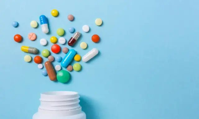 Różnorodne tabletki i kapsułki wysypujące się z białego pojemnika. Czy to opioidy, co to za leki?