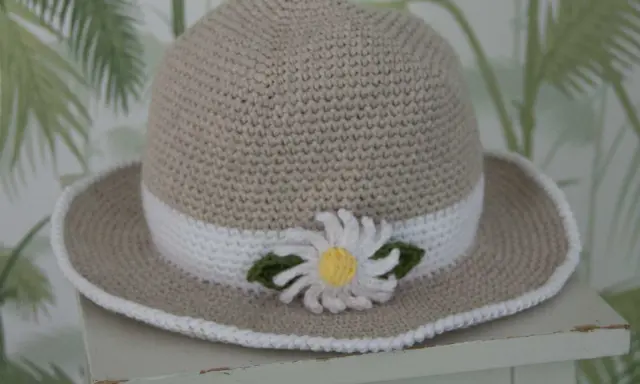 En virkad solhatt för barn, beige med vit kant och en söt blomdekor. Perfekt för soliga dagar!
