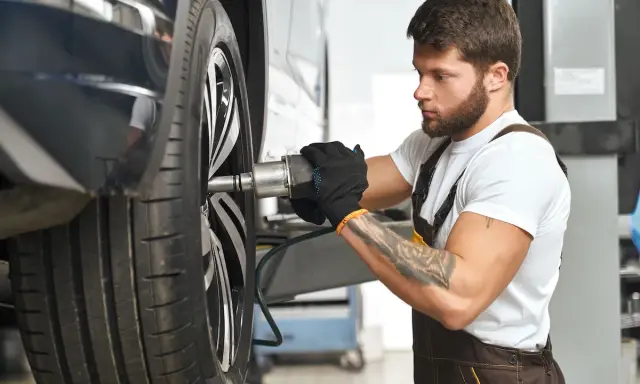 Mechanik z tatuażem dokręca śrubę koła. Zwróć uwagę na objawy zużycia sworznia wahacza, gdy słyszysz stuki.