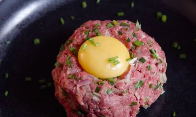 Delicioso steak tartar de wagyu con yema de huevo y cebollino picado, servido en un plato negro.