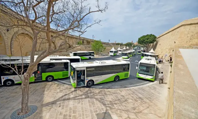 Kolejka zielono-białych autobusów Malta Public Transport czeka na pasażerów. Lotnisko na Malcie tętni życiem.