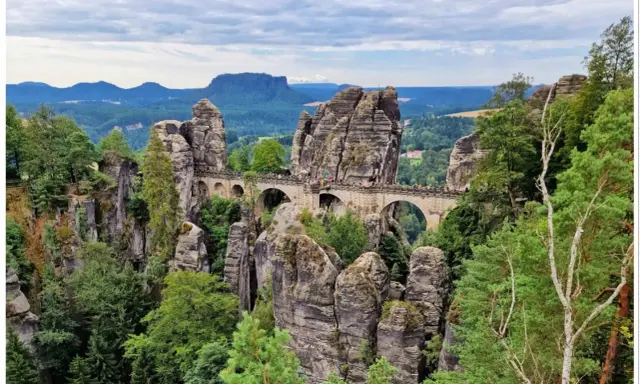 Kamienny most Basteibrücke w Szwajcarii Saksońskiej, łączący skalne baszty pośród zielonych lasów i malowniczych krajobrazów.
