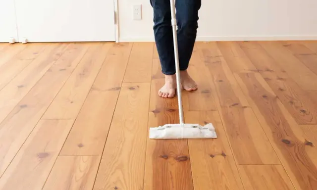 Persona descalza limpiando parquet con una mopa. El suelo de madera luce brillante y cuidado.