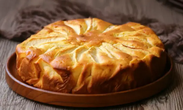 Una deliziosa torta di mele dorata, con le mele disposte a raggiera sulla superficie, pronta per essere gustata.