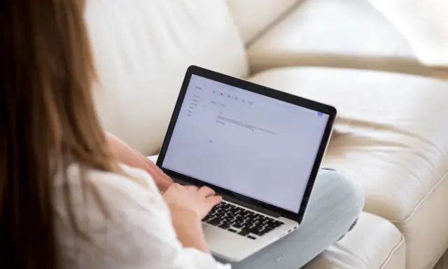 Kobieta pisze maila na laptopie, podkreślając ważne fragmenty tekstu.