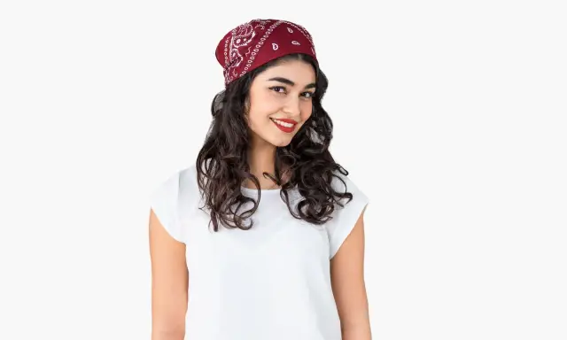 Uśmiechnięta dziewczyna z burzą loków, na głowie ma czerwoną bandana. Pokazujemy, jak zawiązać chustę na głowie.