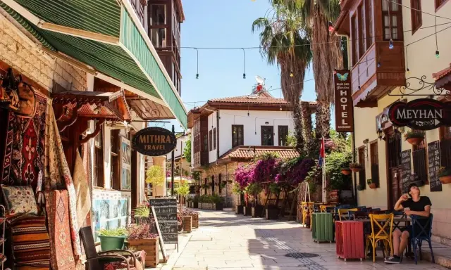 Bunte Gassen in der antalya altstadt mit Teppichläden, Palmen und einem Café, wo ein Mann entspannt sitzt.