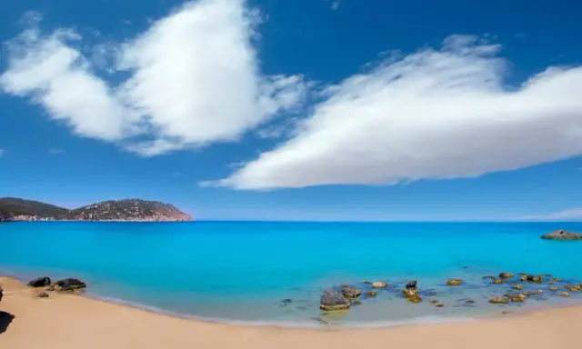 Traumhafter ibiza strand mit türkisblauem Wasser, goldenem Sand und einer felsigen Küste unter einem strahlend blauen Himmel mit weißen Wolken.