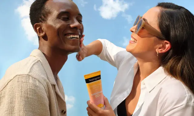 Un homme rit sous le soleil, une femme lui applique de la crème solaire pour protéger son visage.
