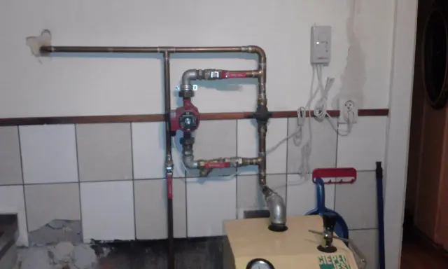 Montaż pompy CO w układzie otwartym. Widoczna instalacja hydrauliczna, czerwona pompa, zawory i fragment kotła.