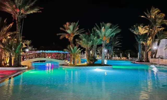 Nocny basen z palmami i mostkiem, idealne miejsce na relaks. Wiele pozytywnych fiesta beach djerba opinie potwierdza jego urok.