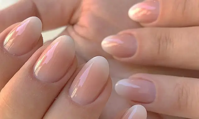 Delikatne, owalne paznokcie z subtelnym, perłowym połyskiem. Klasyczny francuski manicure w nowoczesnym wydaniu, podkreślający naturalne piękno dłoni.