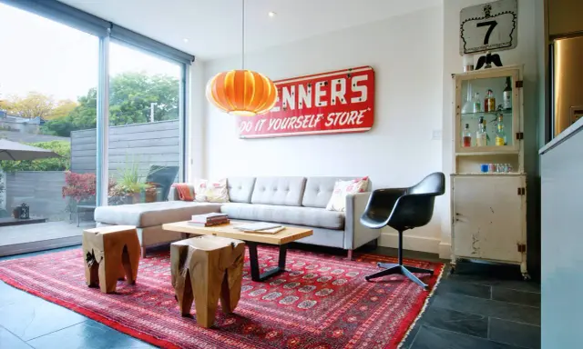 En röd persisk matta ger inspiration till detta vardagsrum med grå soffa, träpallar och en vintage-skylt.