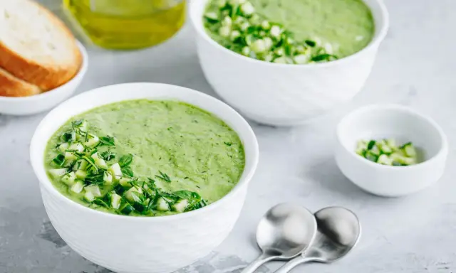 Deux bols de gaspacho concombre frais, garni de dés de concombre et d'herbes. Du pain grillé et de l'huile d'olive à proximité.