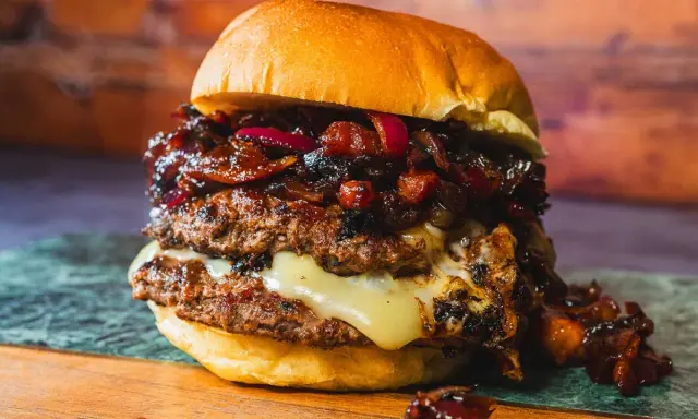 Saftiger Burger mit doppeltem Patty, geschmolzenem Käse und einer süß-salzigen Bacon Jam-Schicht, garniert mit roten Zwiebeln.