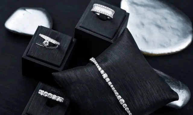 Gioielli scintillanti, anelli e bracciali con diamanti, esposti su supporti neri e pietre levigate.
