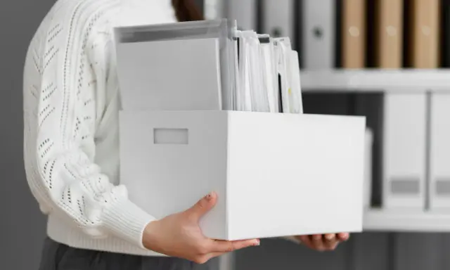 Osoba trzyma białe pudełko z dokumentami, ułatwiające przechowywanie dokumentacji pracowniczej.