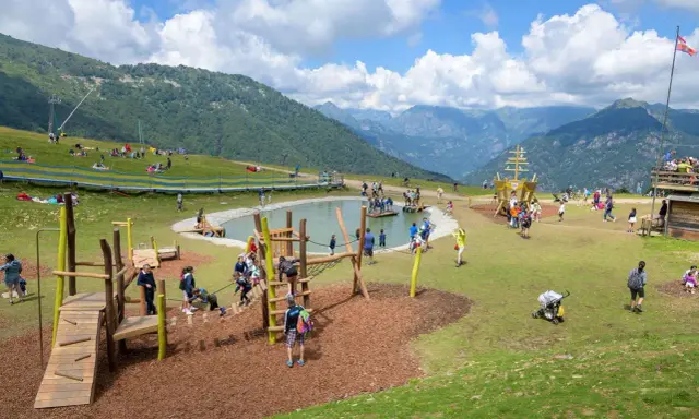 Un parco giochi in montagna con un laghetto, un galeone e tante famiglie che si divertono. Perfetto per le vacanze in montagna con bambini.