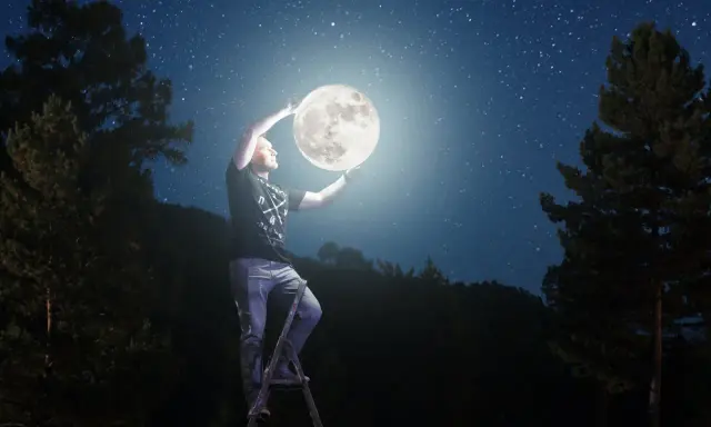 Mężczyzna na drabinie trzyma księżyc, marząc o studiach z astronomii. Nocne niebo pełne gwiazd.