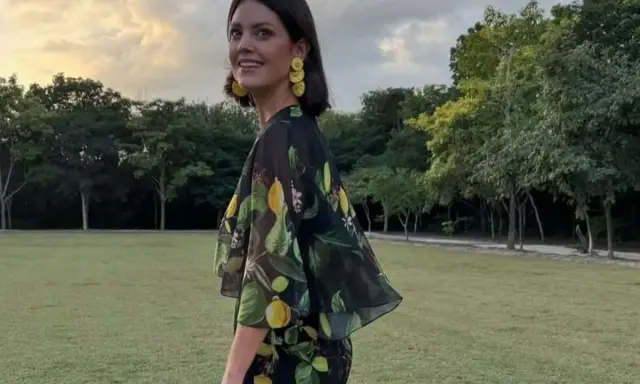 Isabelle Junot sonríe con un vestido estampado de limones, luciendo pendientes amarillos y un sombrero de paja en un día soleado.